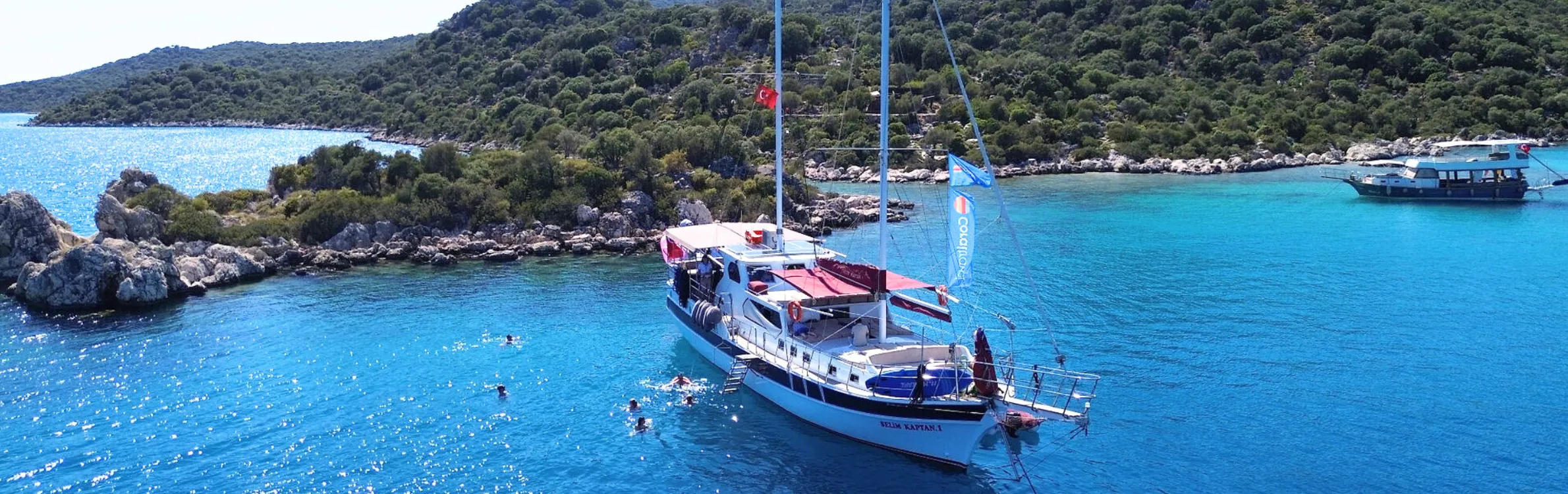 Boot mit Türkeiflagge steht an einer Bucht und Menschen schwimmen im Meer