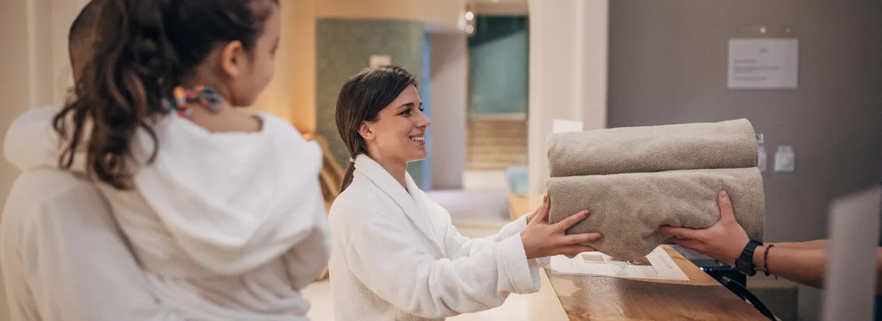 Eine Frau grinst und bekommt Handtücher in die Hand im Spa