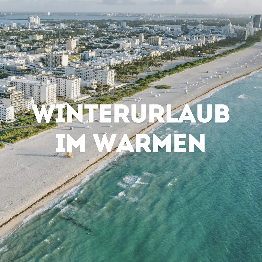 Familie mit hellen Klamotten steht am Strand und schaut auf das Meer